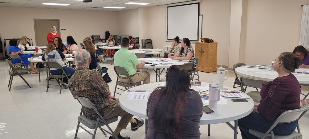 A group of people sitting at round tables listening to a speaker